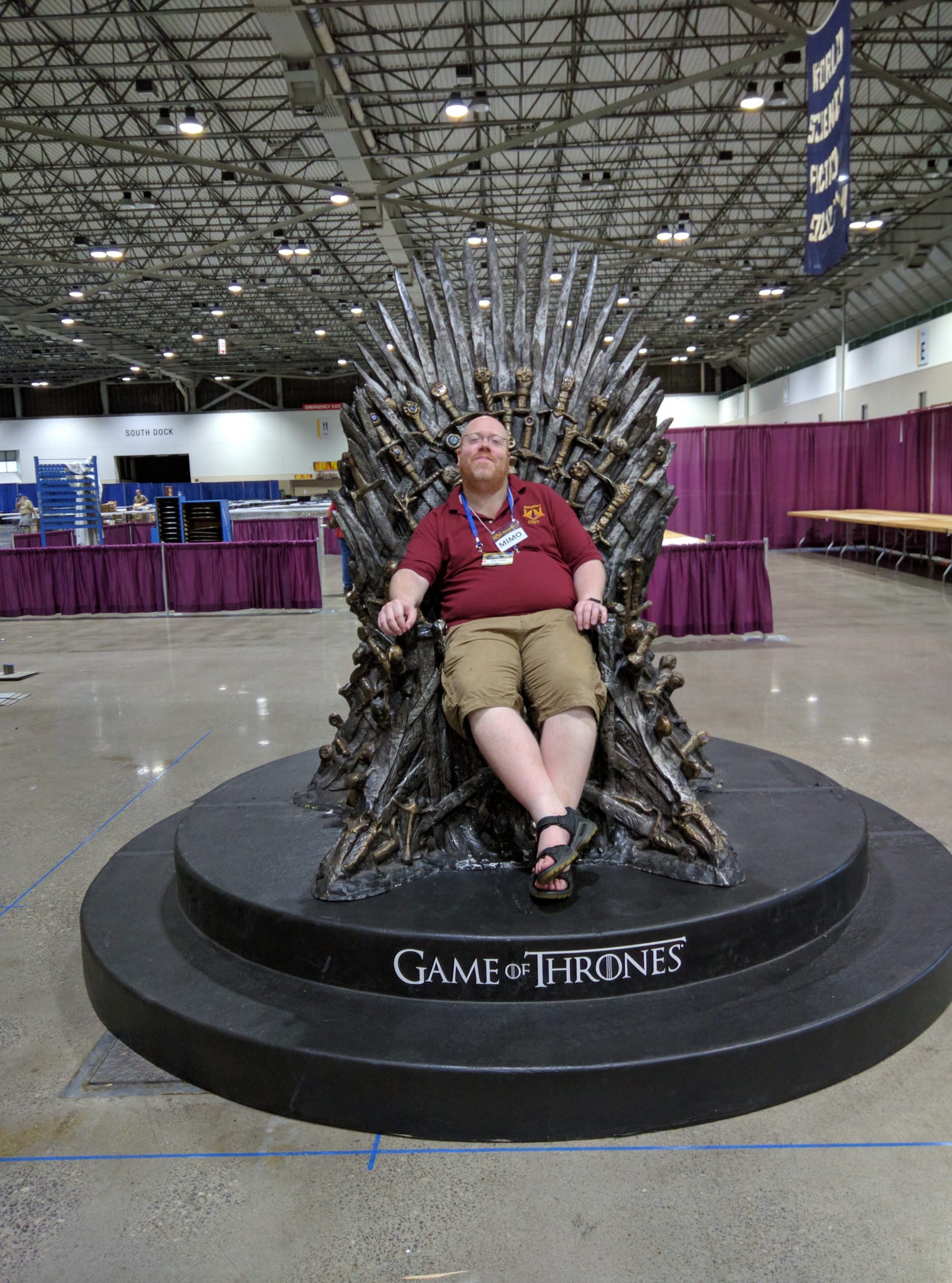 Brian Nisbet sitting in a replica of the iron throne from the TV show Game of Thrones, with a large convention venue in the background