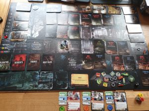 The 'This War of Mine' board, featuring a large darkly coloured board with various cards, character pieces, prompts, and tokens.