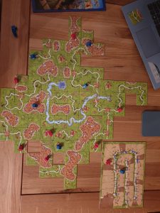 Photo of the game board; many different square tiles placed next to one another to create a scene of green fields, castle perimeters, and blue rivers.
