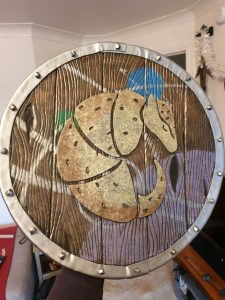 photo of the completed foam shield with wood grain effect and an overlaid armadillo design