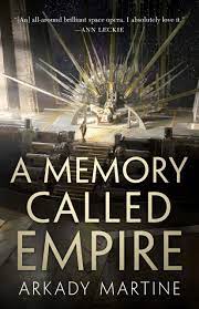 The image shows the cover of A Memory Called Empire by Arkady Martine. The image is a wide view of a throne room with steps leading up to a throne. The throne is styled to look like the rays of a radiant run. On the throne a person in a white robe sits. Another person stands at the top of the throne facing it. The bottom half of the image is overlaid by the title and authors name in a gunmetal golden font.