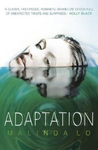 The image shows the cover of Malinda Lo's novel 'Adaptation'. The cover is split into 1 third white (this is the top) and 2 thirds green. In the white third a face with pale skin and wet slicked back hair rises up out of the green third. The green thrid is made too look like rippling water on which the face is reflected. 