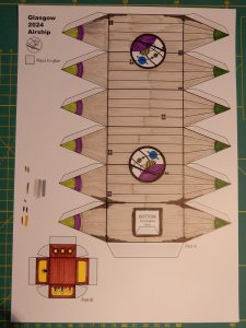 Printout of airship design, coloured with felt-tip pens - grey balloon with violet and green Glasgow logo, and a brown gondola with yellow light coming out of the windows.