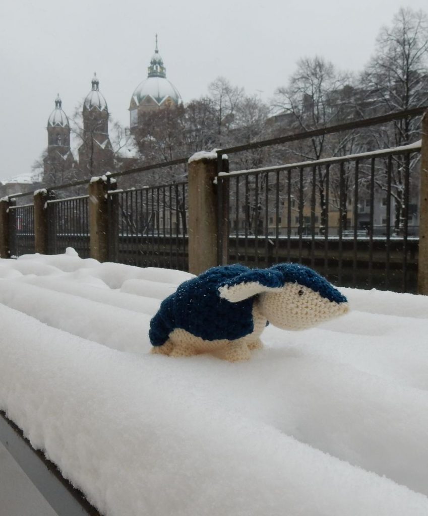 Berta the crochet armadillo sitting on a snowed-in bench in Munich.