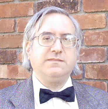 A portrait photograph of Ben Yalow, a middle-aged man wearing glasses, a grey suit and a chequered navy bow tie