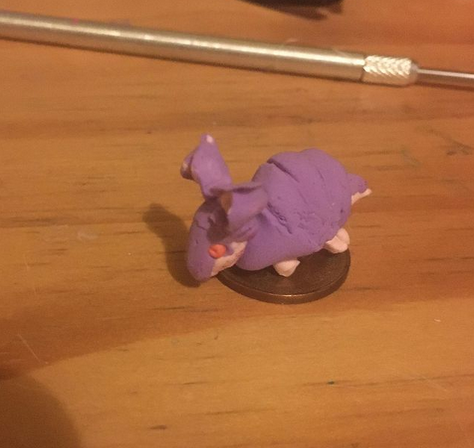 A tiny light pink armadillo with purple armour sitting on a small coin.