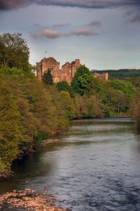 photograph of an imposing castle on a forested riverbank, lit by the setting sun