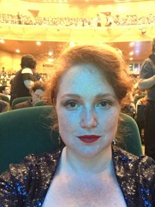 Marguerite at the Hugos in Dublin 2019. A smiling woman with auburn hair and red lipstick in a glittering black top, looking made up and ready for an event.