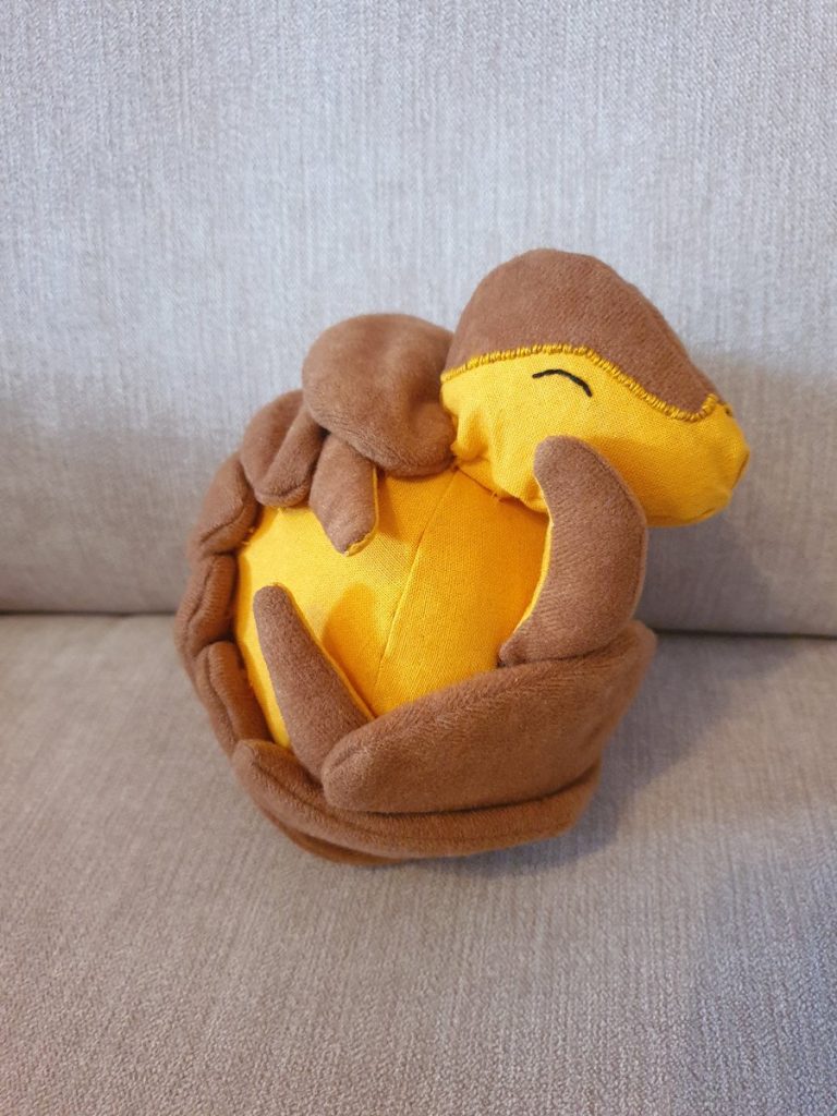 Armadillo plushie, rolled up. The body is bright yellow, the armour is brown. The eye is closed.