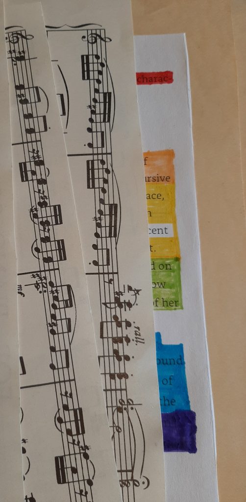 The image shows sheet music over the edge of a text document where large sections of the text have been obscured using a rainbow of coloured pens.