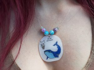 Close up of Space Whale necklace, worn. A bit of hair, neck and clevage is visible.