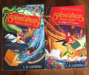 The image shows the covers of L.D. Lapinski's novels The Strange Worlds Travel Agency and The Strange World's Travel Agency - Edge of the Ocean. The first books shows a female figure in ref top and blue jeans flying unaided on a background of stars, planets, and books, with what looks to be magical traveling trunks. There is a green tentacled creature in the top left hand side. The second book cover shows the same girl gripping the handle of a suitcase as she repels away from a wooden sail ship cross a frothy ocean, tentacles reach out of the water. 