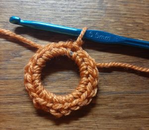 Keyring with one round of single crochet in orange worked around it. in the open loop there's a bright blue crochet hook.