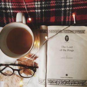 A copy of the Lord of the Rings open at the title page, surrounded by fairy lights, a mug of tea, autumn leaves, and a pair of glasses. Image credit Madalena Dalezieu 