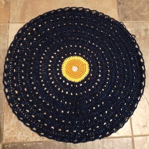 Round piece of navy crochet with orange and yellow sun in the middle.