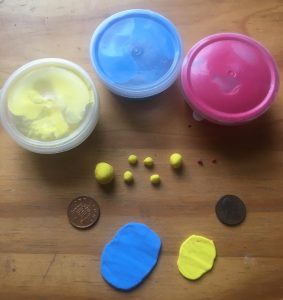 Materials for polymer clay armadillo: three tubs of clay in yellow, blue and pink at the top, several balls of yellow and pink already formed below, and two pieces rolled out flat in blue and yellow at the bottom. Left and right: two pennies for scale.