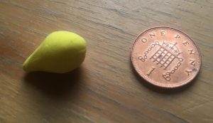 On the left, a pear-shaped piece of yellow clay, length about the diameter of a penny, on the right, penny for scale.