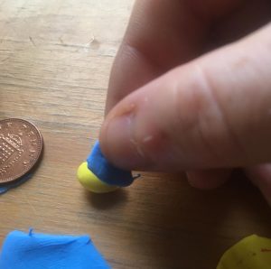 A small piece of the blue sheet of polymer clay is being wrapped around the yellow head form.