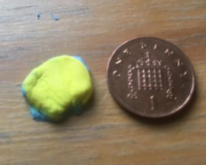 Cut out circle from the blue and yellow sheet of clay, significantly smaller than the penny shown for scale.