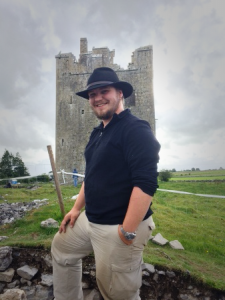 photo of Jay Hall, wearing a black shirt and black hat, in front of Castle Stalker