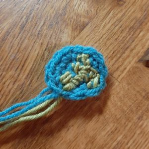A light blue crochet circle with random green embroidery stitches on top.