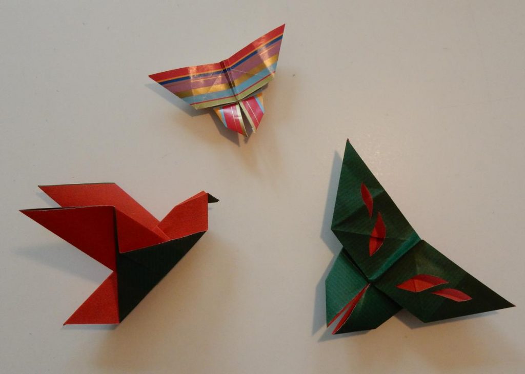 Three origami pieces - on the top a butterfly made from striped wrapping paper, below left a bird from red and green paper, on the right another butterfly from the same red and green paper.