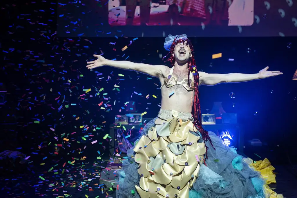 A performer in costume on stage with confetti falling around them.