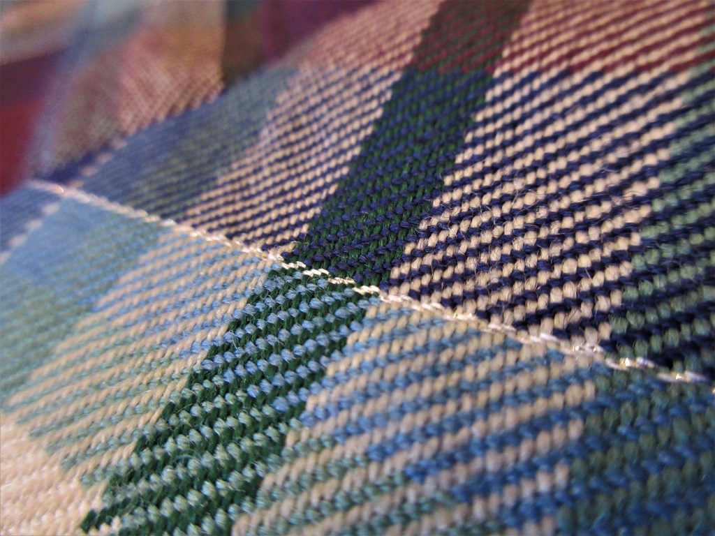 A close-up detail of tartan-patterned fabric in purple, dark blue and light blue, grey, and cream. 