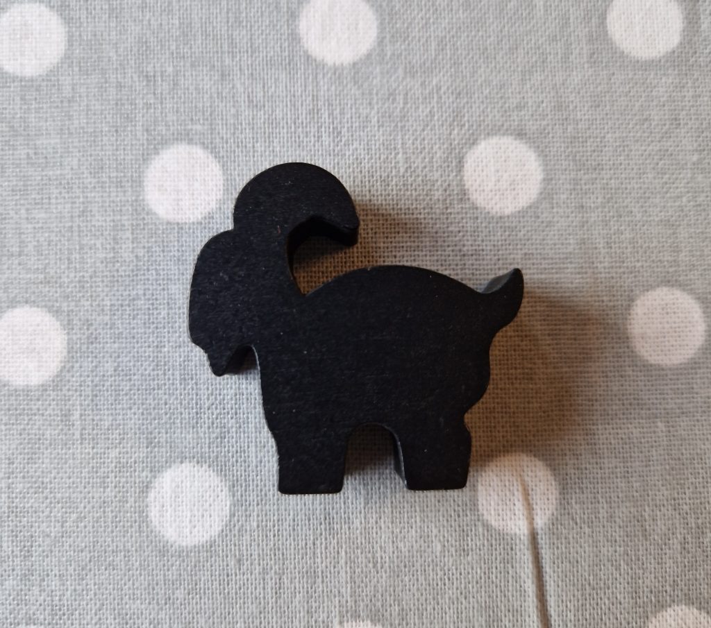 A black wooden mountain goat moving piece sits atop a polka-dot patterned cloth. 