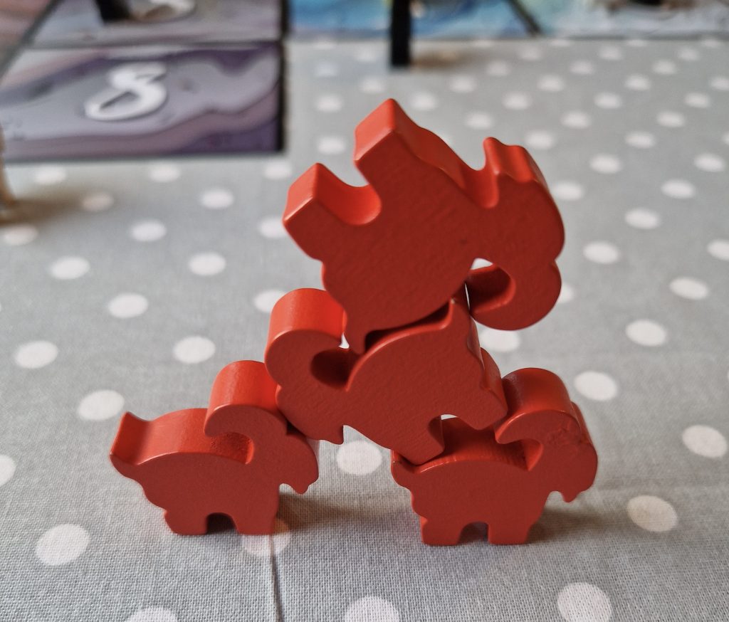 Four red wooden mountain goat moving pieces stacked in a pyramid-type shape. They are sitting atop a polka-dot patterned cloth. 