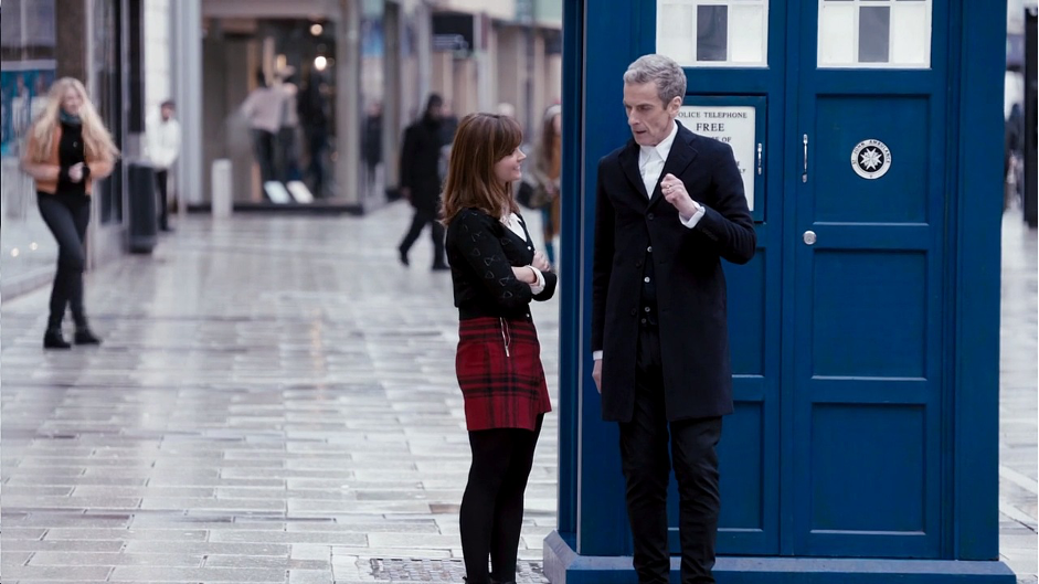 “The Twelfth Doctor (Peter Capaldi) and his companion Clara (Jenna Coleman) stand next to a blue police box.”