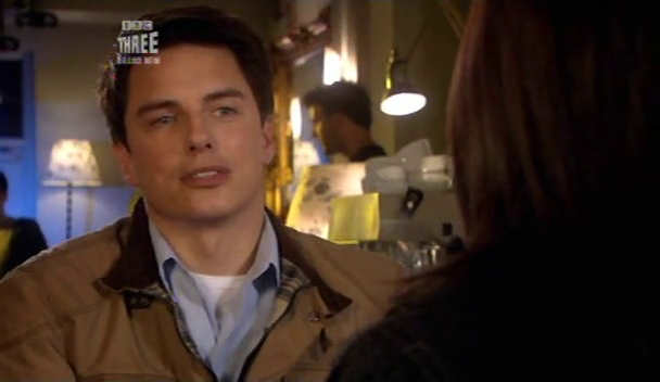 “Jack Harkness (John Barrowman), wearing a brown jacket, is engaged in conversation with Gwen Cooper (Eve Myles)”