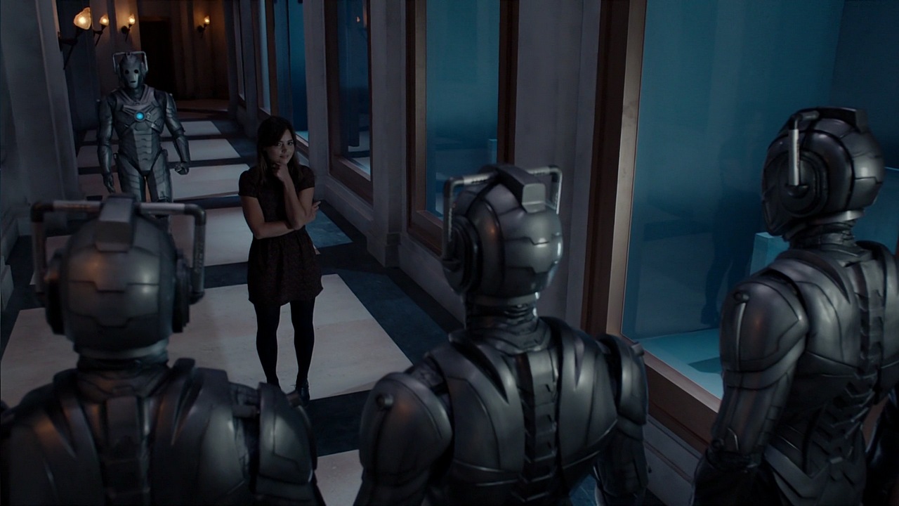Clara (Jenna Coleman) faces three Cybermen in a hallway. Another Cyberman stands behind her.”