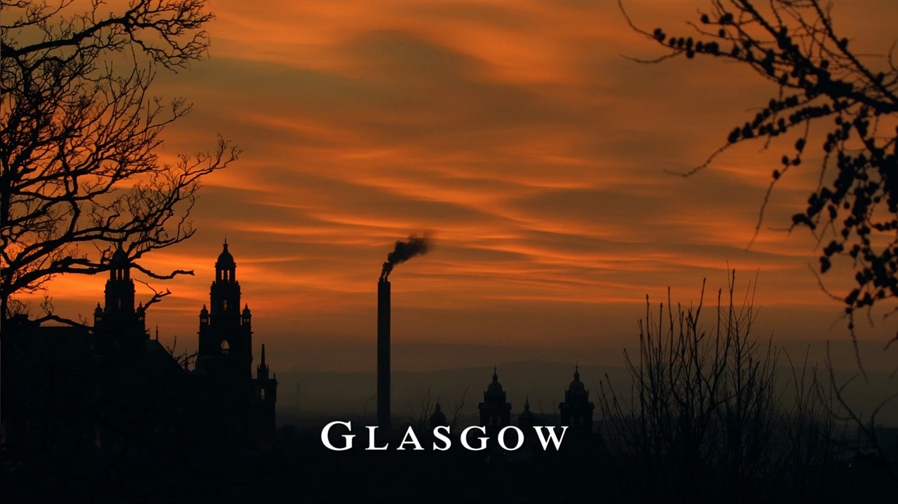 “An orange cloudy sky set above the spires of the Kelvingrove Art Museum and foliage. White text displays the word 'Glasgow'.”