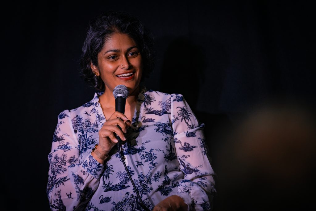 A woman is smiling and speaking into a microphone.